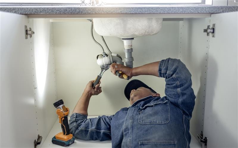 Plumber repairing pipes beneath a bathroom sink in Estero