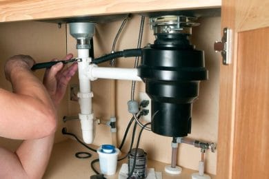 Plumber repairing a garbage disposal beneath a kitchen sink in Estero