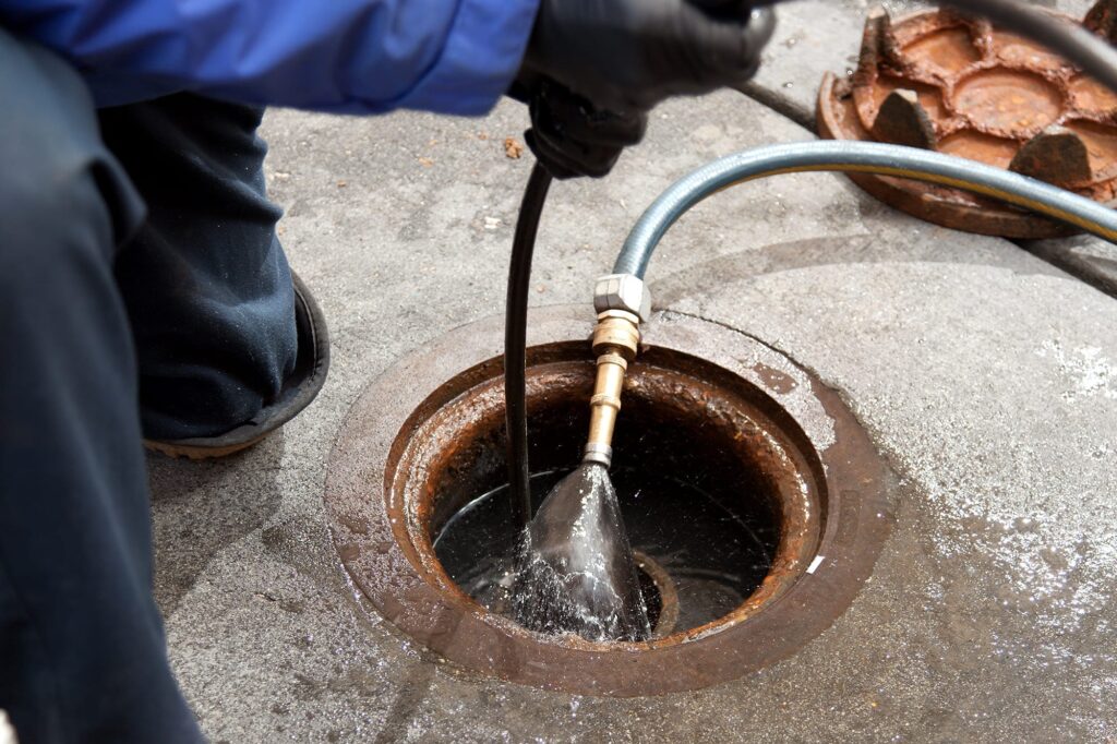 Plumber hydro jetting a sewer line through a manhole in Estero
