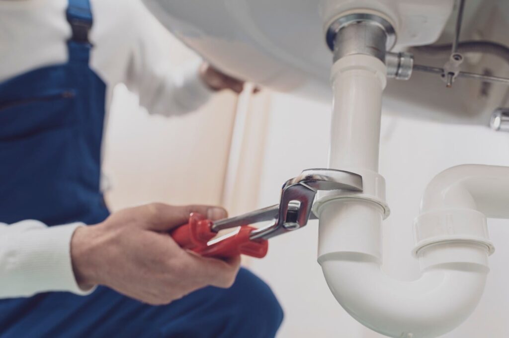 Plumber repairing a white drain pipe beneath a sink in Estero
