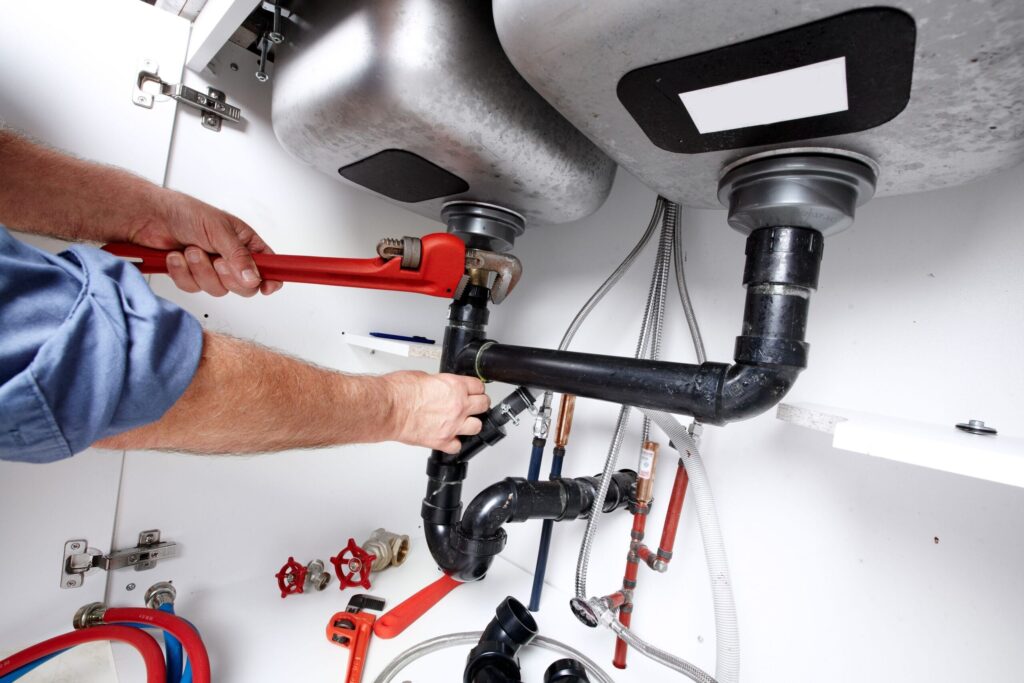 Plumber repairing drain pipes beneath a kitchen sink in Estero