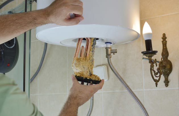 Technician removing mineral buildup from a water heater in Estero